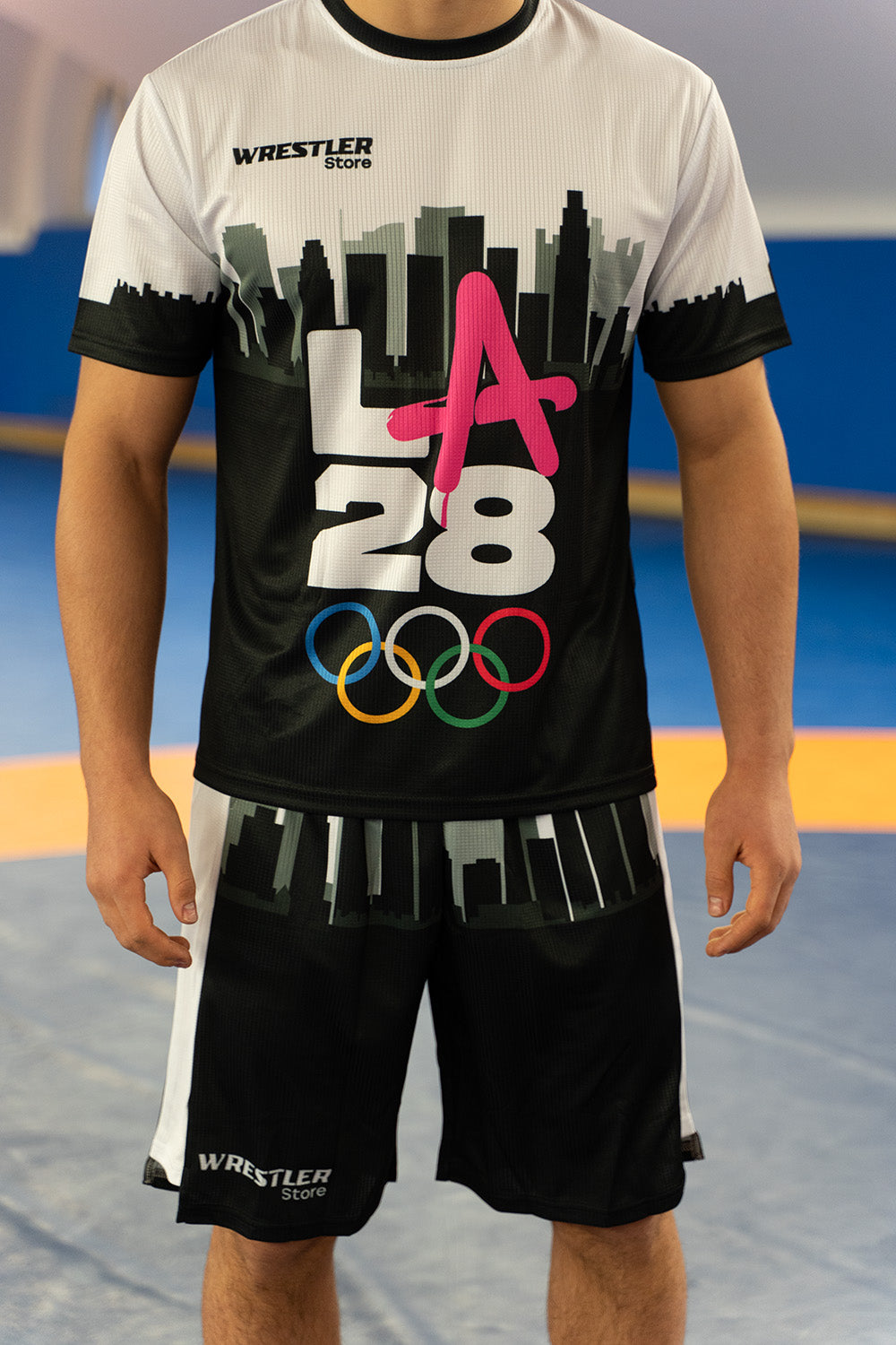 Model trägt WrestlerStore T-Shirt & Shorts Set im LA 2028 Design mit langlebigem Sublimationsdruck auf der Matte im WrestlerStore