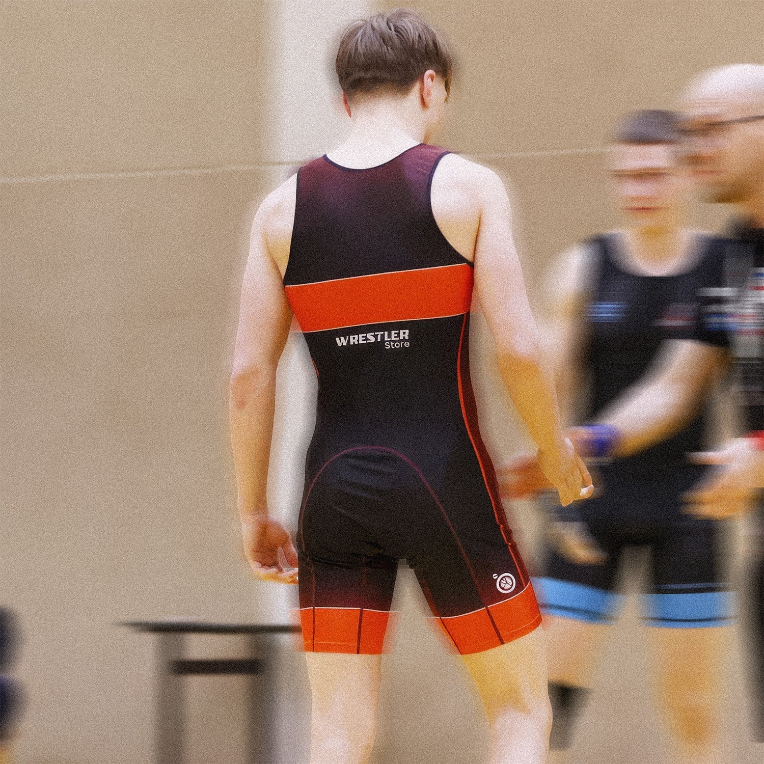 Junger Ringer von hinten in einem schwarz-orangenen WrestlerStore-Singlet bei einem Wettkampf – Vorschaubild zum Blogbeitrag über Knie- und Schulter-Prävention im Ringen.